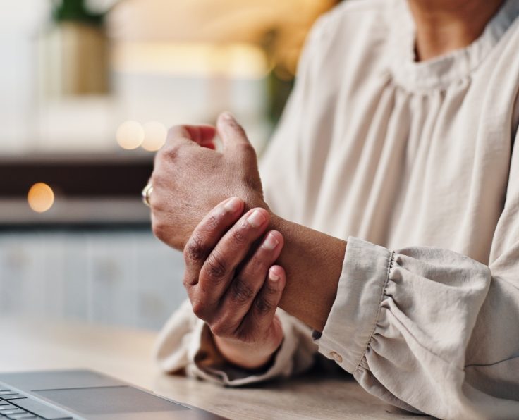 Arthritis, hands and laptop with business person at desk in office for administration or typing rep