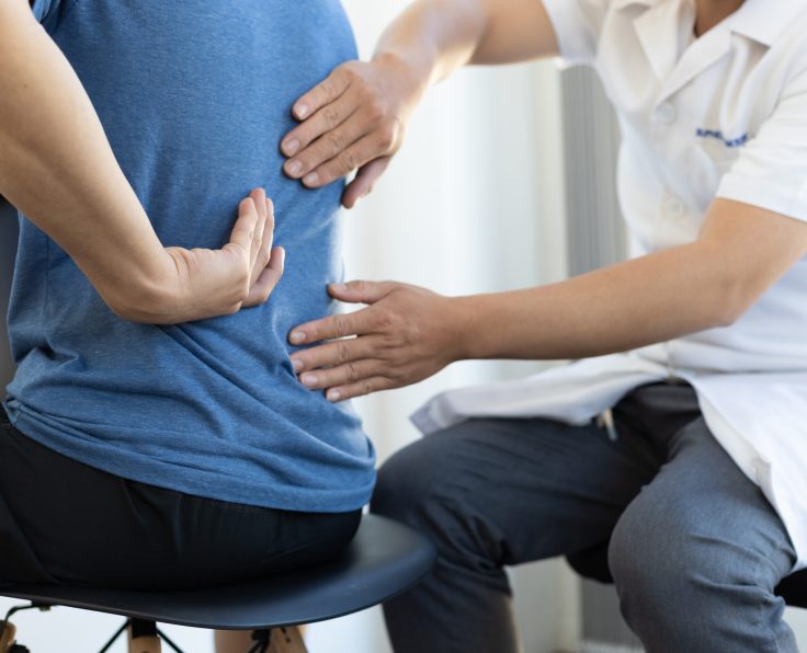The doctor is diagnosing the patient's back pain. A male with back pain sees a doctor for treatment.