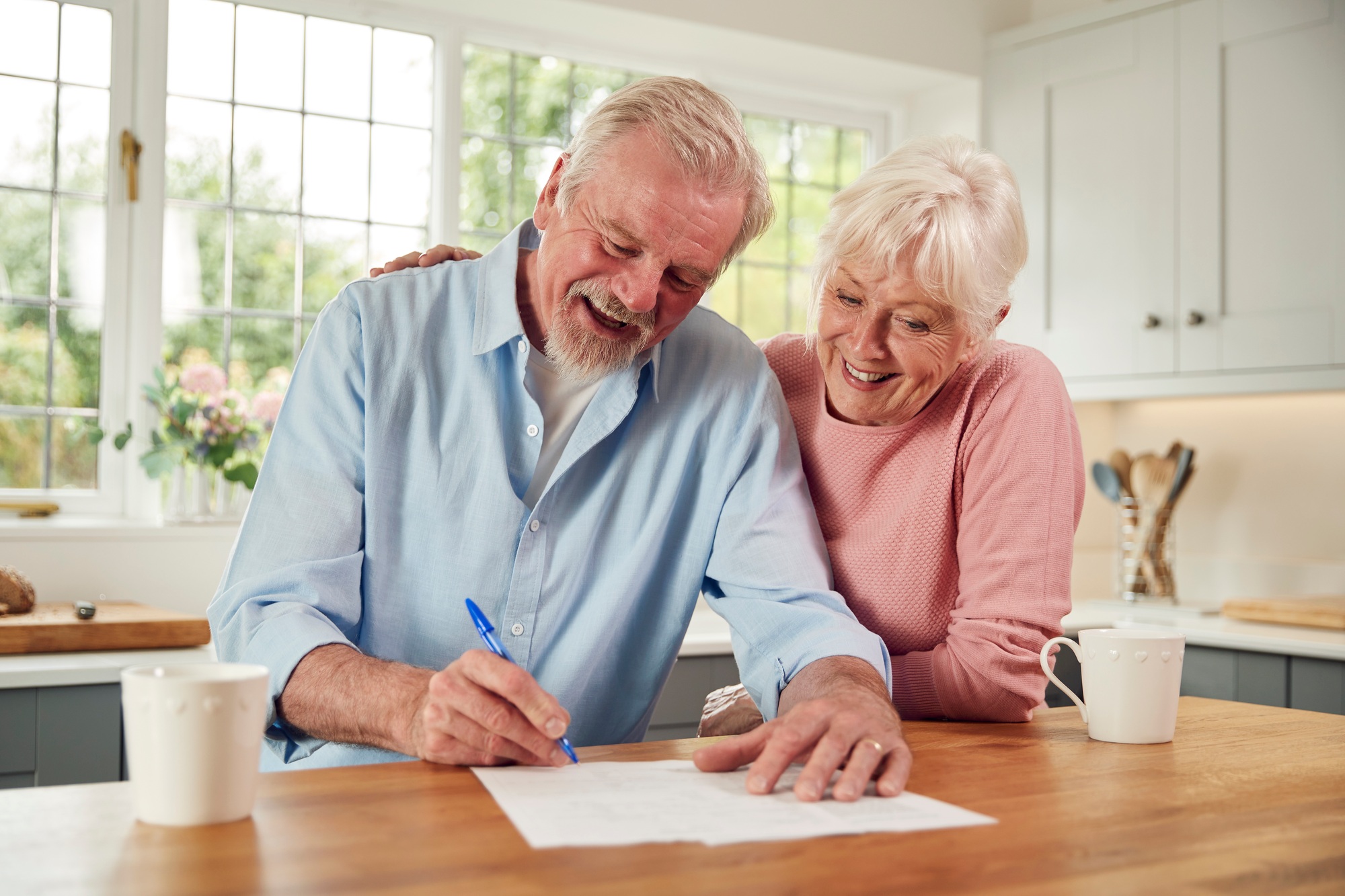 Retired Senior Couple Sitting In Kitchen At Home Signing Financial Document
