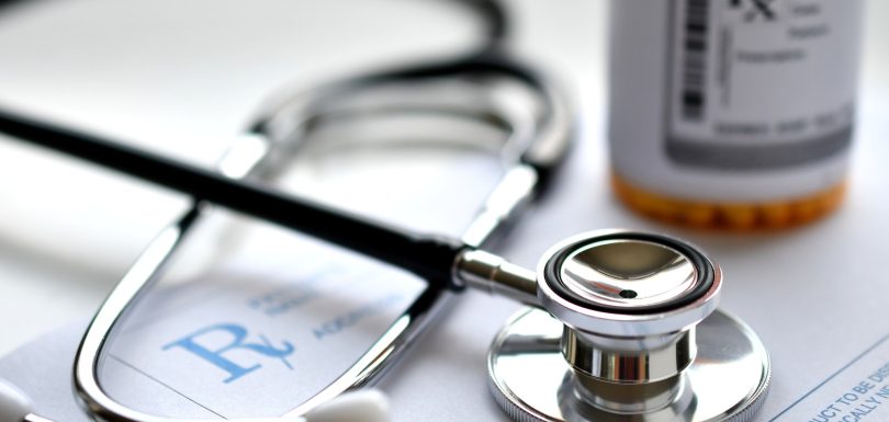 A doctor's stethoscope on a prescription RX pad with a bottle of medicine, pharmacy pharmaceuticals