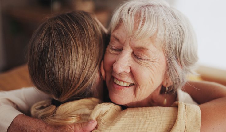 Woman, love and hug senior mom in home for mothers day, bonding and visit in retirement with care or happy. Person, smile and embrace with elderly parent for reunion, comfort and affection in hospice