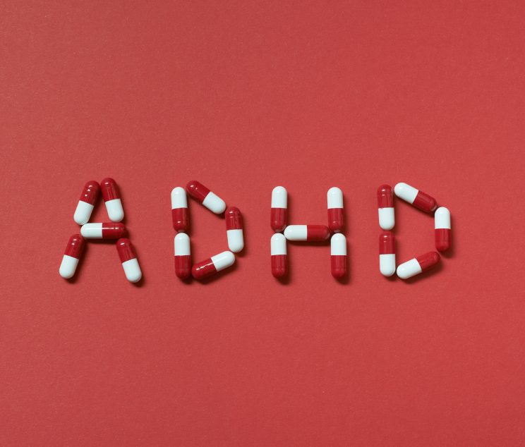 ADHD abbreviation formed of pharmaceutical pills on red background. Attention deficit hyperactivity disorder and mental health awareness.