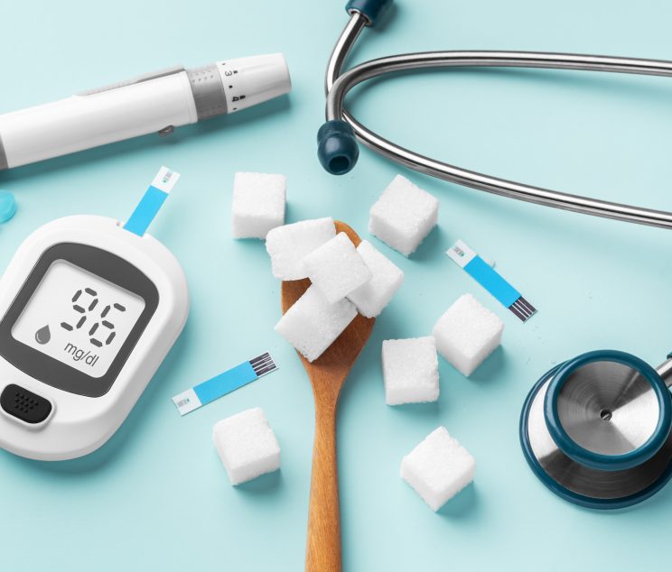 Sugar cubes in spoon with blood glucose meter, lancet and stethoscope on blue background