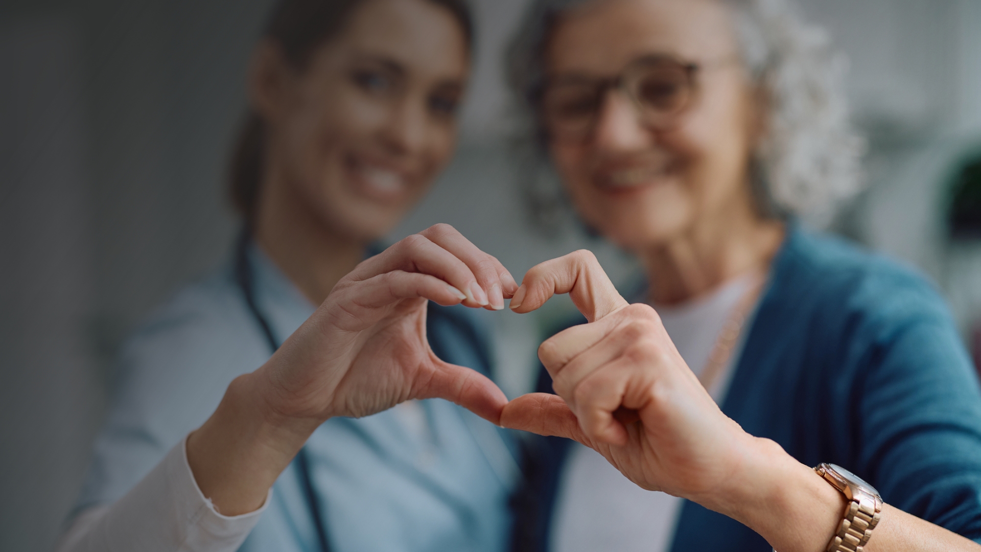 Nursing assistant and older adult forming a heart shape with their hands.